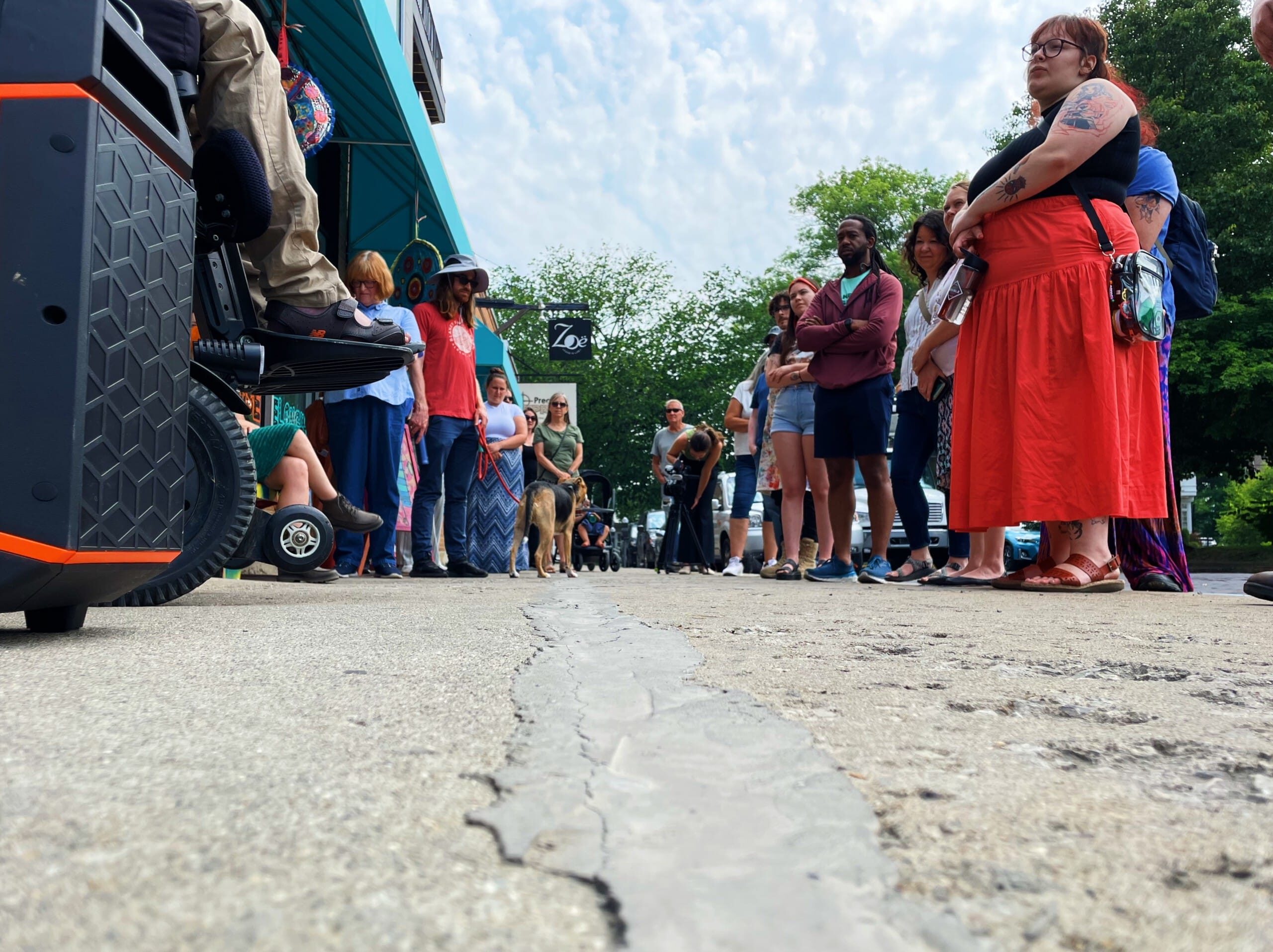 A crowd gathers along the sidewalk on a cloudy summer day.
