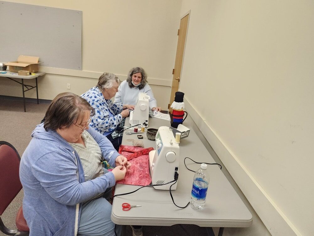 People sit at a table together, using sewing machines.