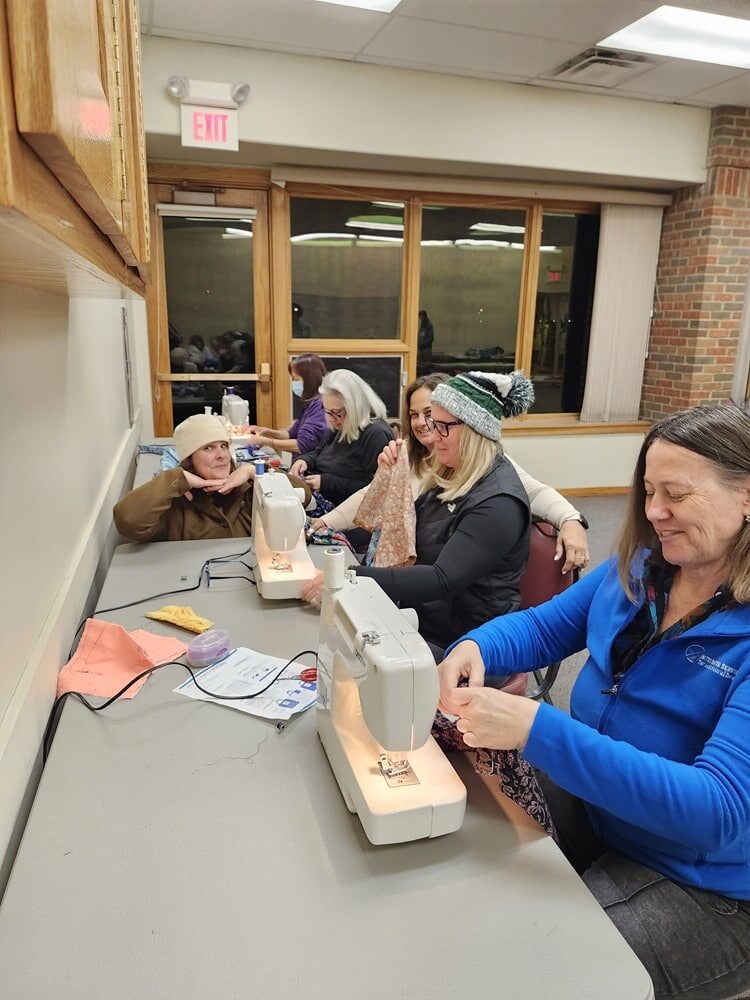 People sitting together at a table, sewing. 