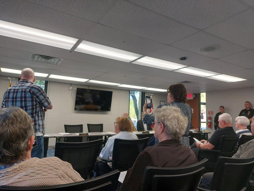 A man in blue plaid stands out before an audience.