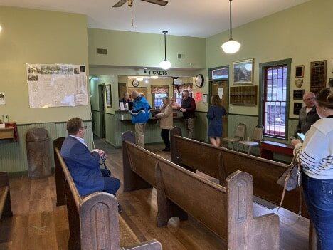 People sit in the train depot on pews.