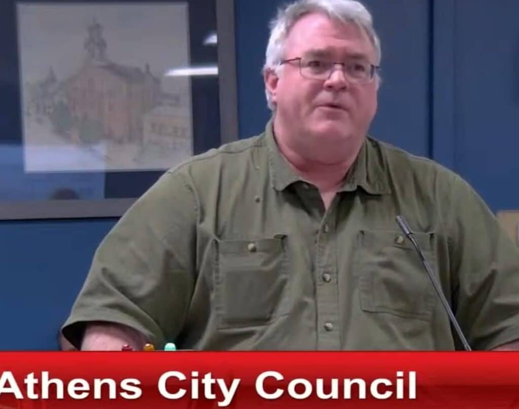 Man in green button-up shirt stands behind a podium. 