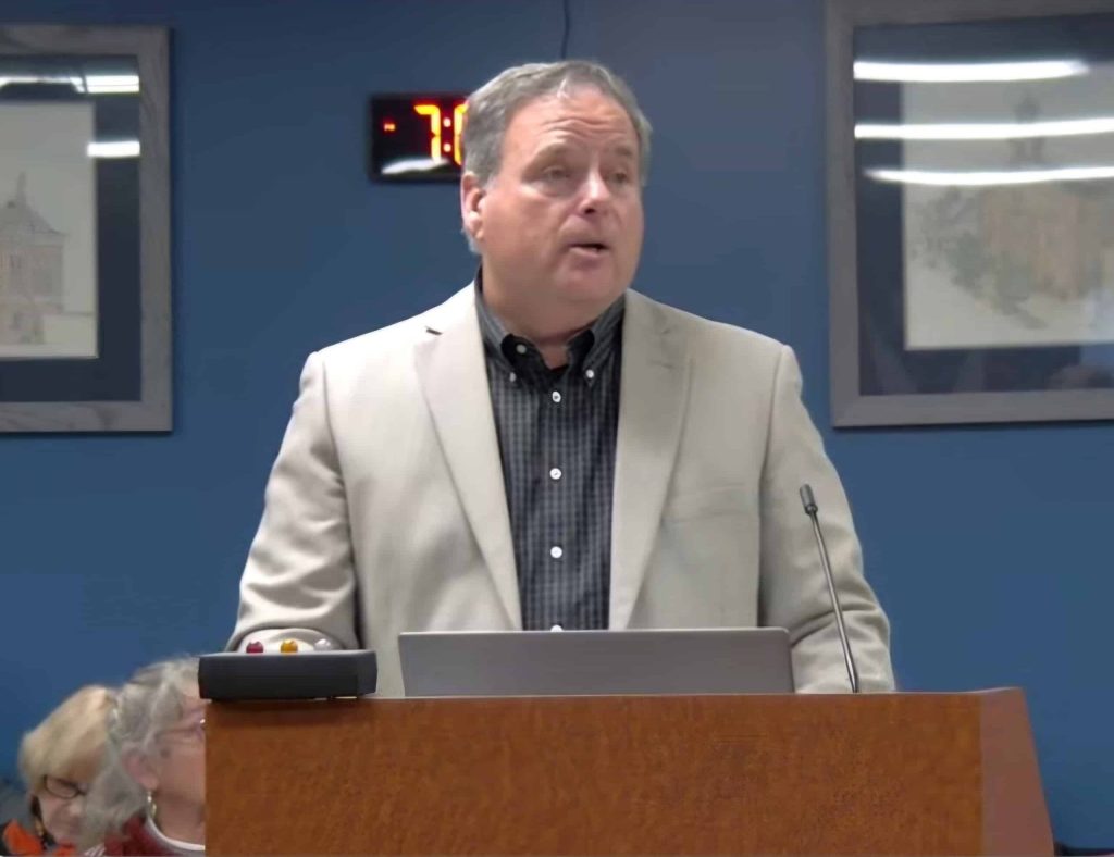 Jerry Miller stands, speaking before a podium.
