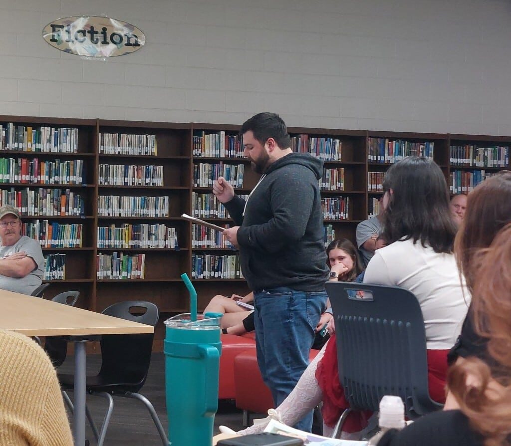 A man stands before a crowd holding a paper from which he reads.