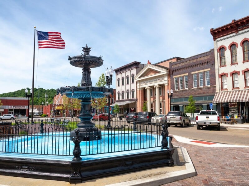 A bright photo featuring an American flag, historic storefronts and the fountain in Nelsonville's Public Square.