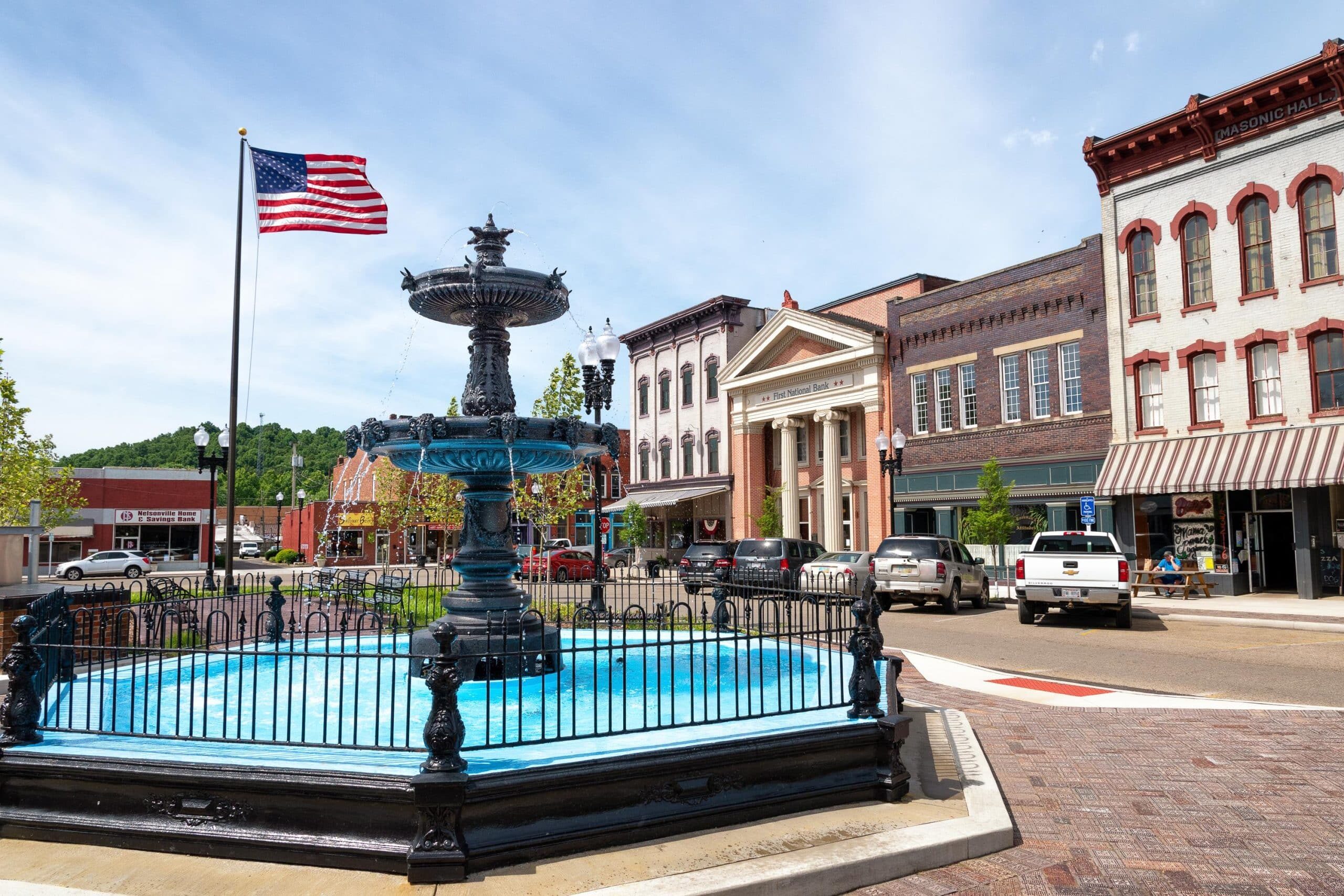 A bright photo featuring an American flag, historic storefronts and the fountain in Nelsonville's Public Square.