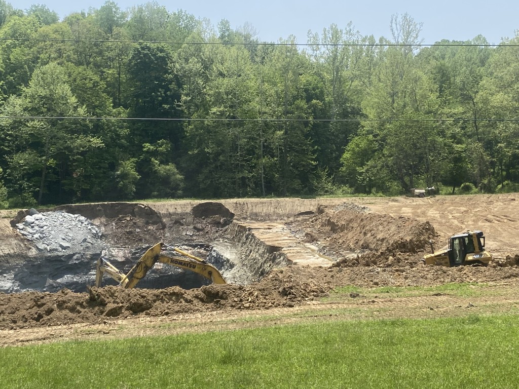 Photo of the Johnson Run strip mine, taken from the roadside on a sunny summer day. A tractor enters the mine while another machine, mostly obscured, works at the bottom.