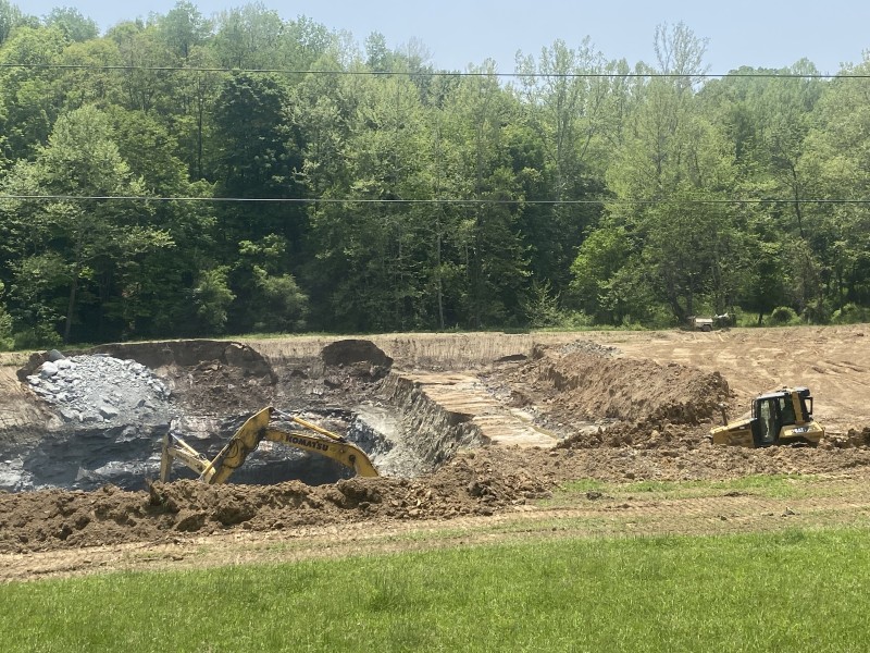 Photo of the Johnson Run strip mine, taken from the roadside on a sunny summer day. A tractor enters the mine while another machine, mostly obscured, works at the bottom.