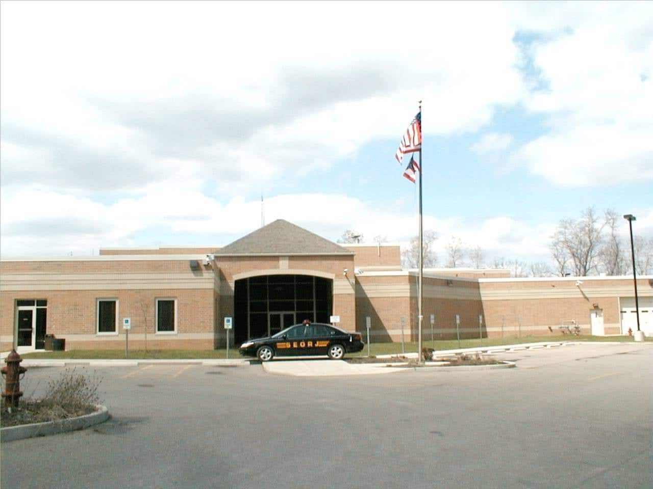 Photo of the front of the Southeast Ohio Regional Jail on a sunny day. A flag waves above the jail entrance, where a cruiser marked 'SEORJ' is parked.