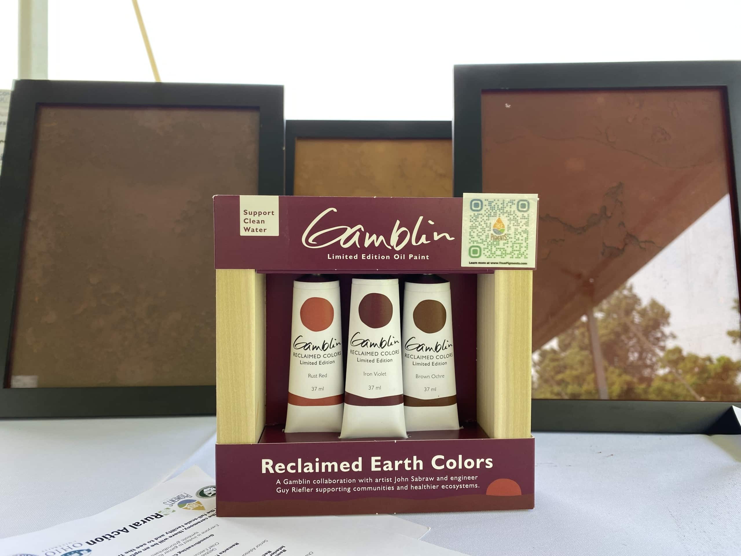 A box featuring three paint tubes labeled ‘Gamblin’ sit in front of three frames displaying the corresponding pigments: Rust Red, Iron Violet and Brown Ochre.