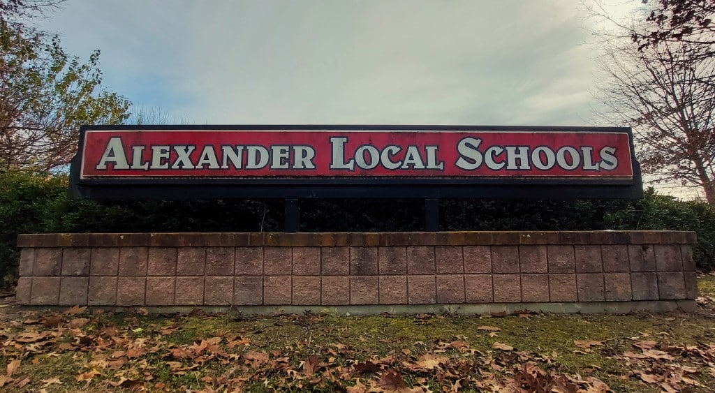 A red sign with white text reads "Alexander Local Schools".