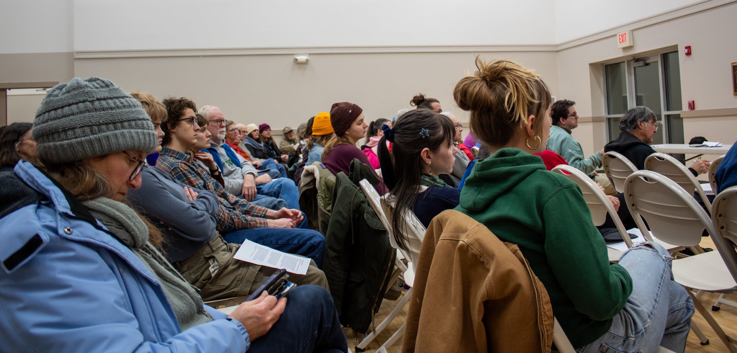 Rows of people sitting in chairs facing the same direction, to watch panelists at a public meeting.