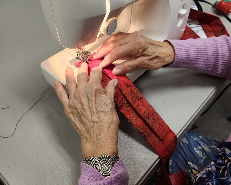 Two hands run a machine sewer on bag straps.