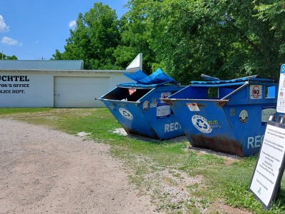 Text on the village building reads "Buchtel Mayor's Office Police Dept." and two large blue recycling bins sit before it.