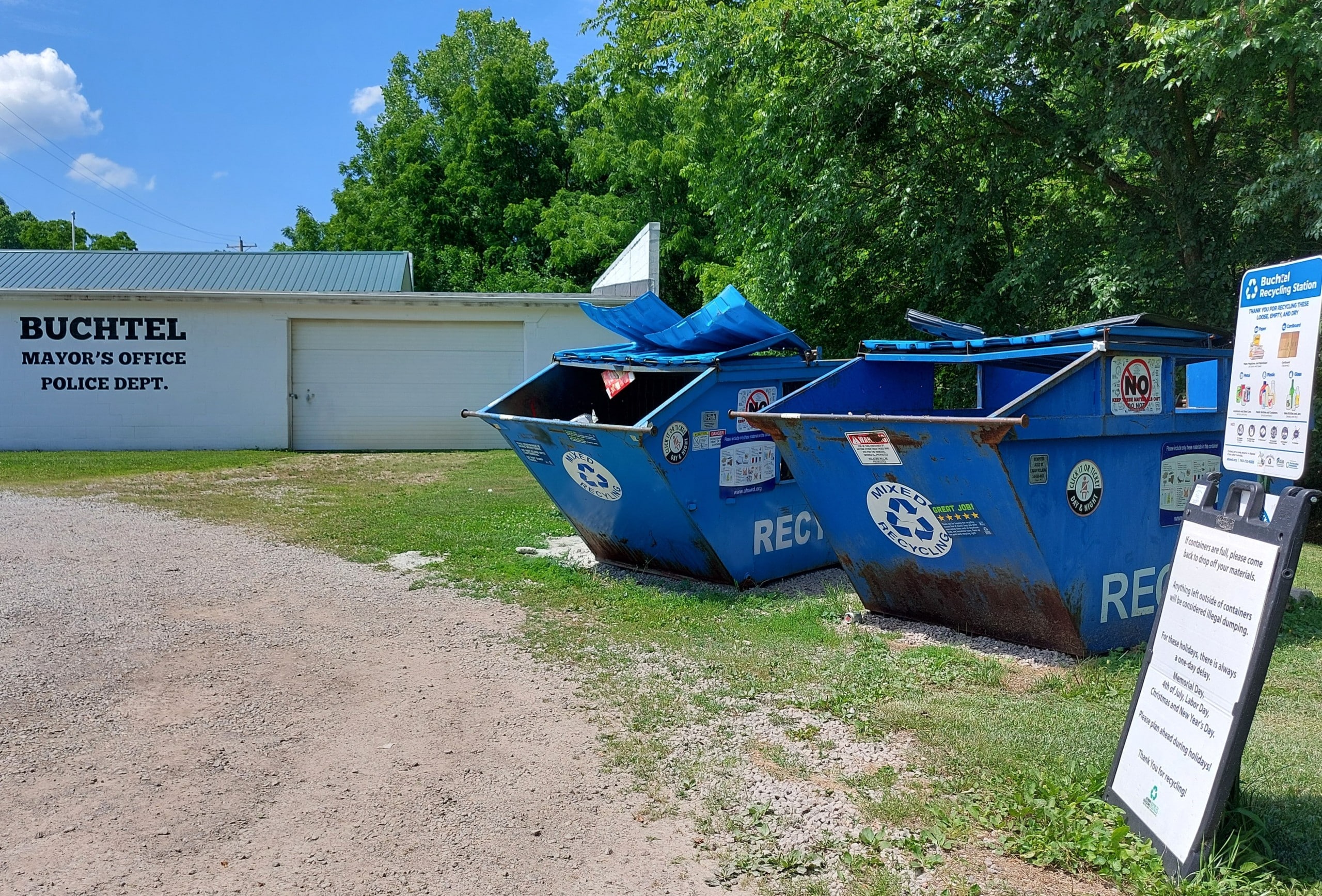 Text on the village building reads "Buchtel Mayor's Office Police Dept." and two large blue recycling bins sit before it.