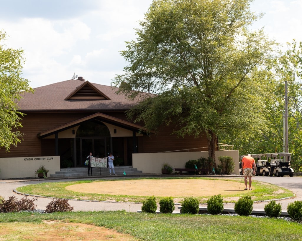 A man golfs in front of the country club.