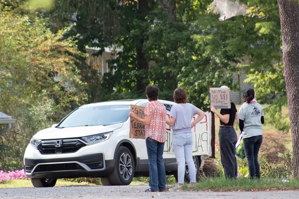 Protestors stand before a white car.