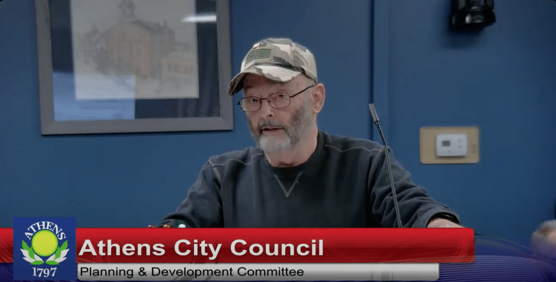 Person in hat stands behind a microphone.