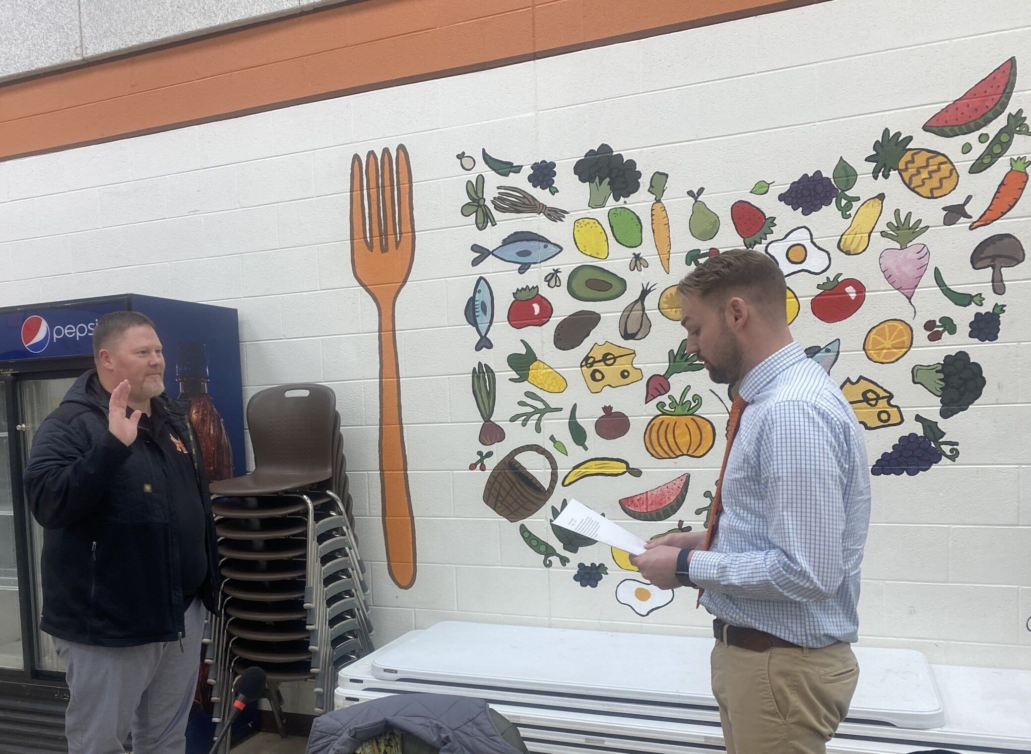 Two men stand, one with his hand raised as the other reads an oath from paper.