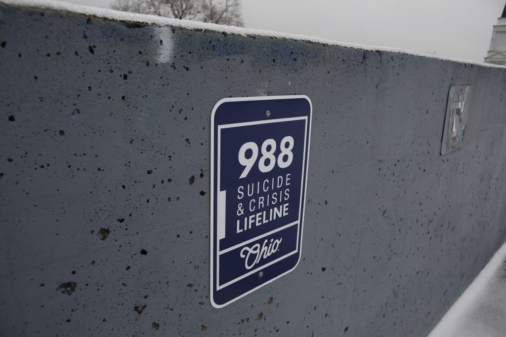 A blue sign on a cement wall reads: 988 Suicide & Crisis Lifeline Ohio.