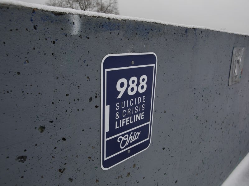 A blue sign on a cement wall reads: 988 Suicide & Crisis Lifeline Ohio.