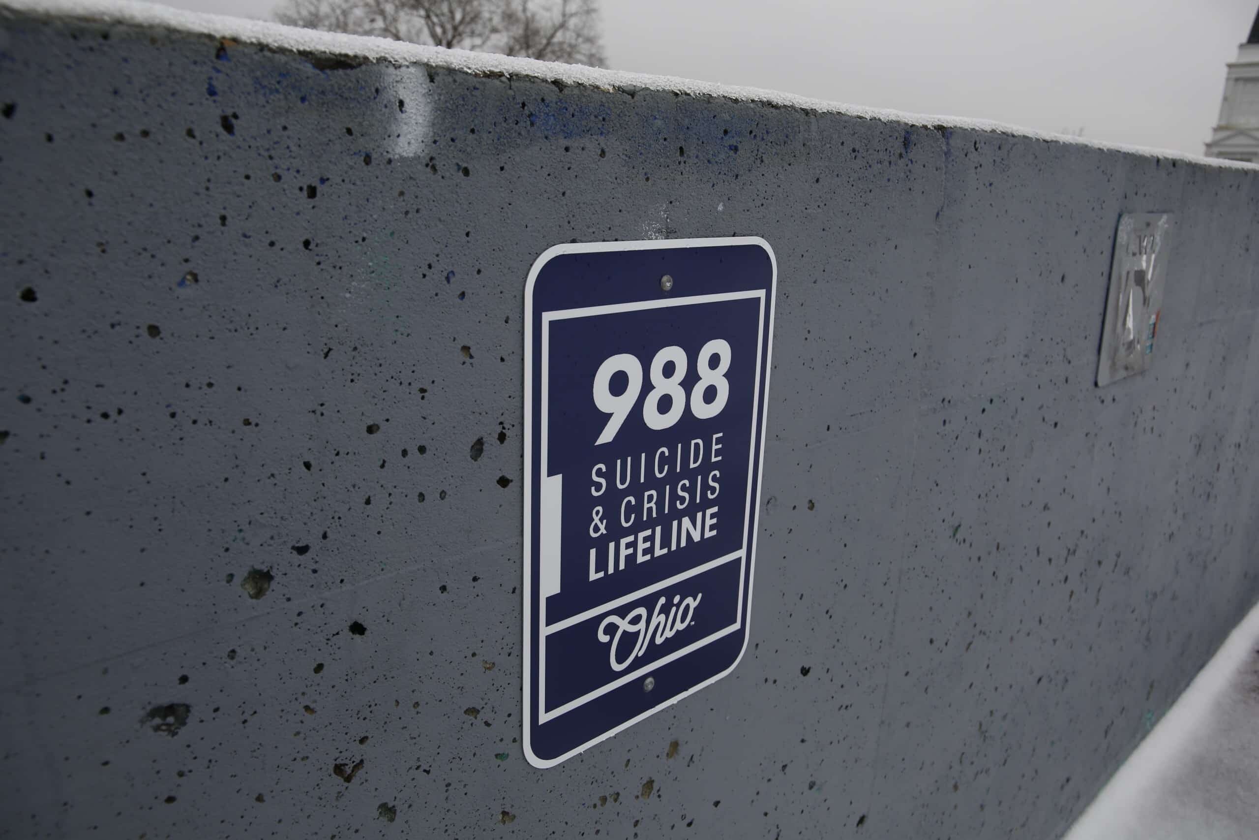 A blue sign on a cement wall reads: 988 Suicide & Crisis Lifeline Ohio.