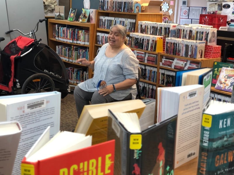 A woman, seated, speaks amongst shelves of library books.