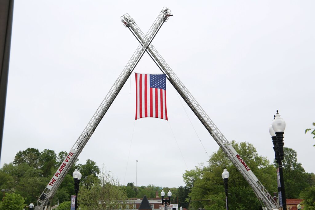 An American flag hands between the ladders of The Plains VFD and Nelsonville FD's fire trucks.