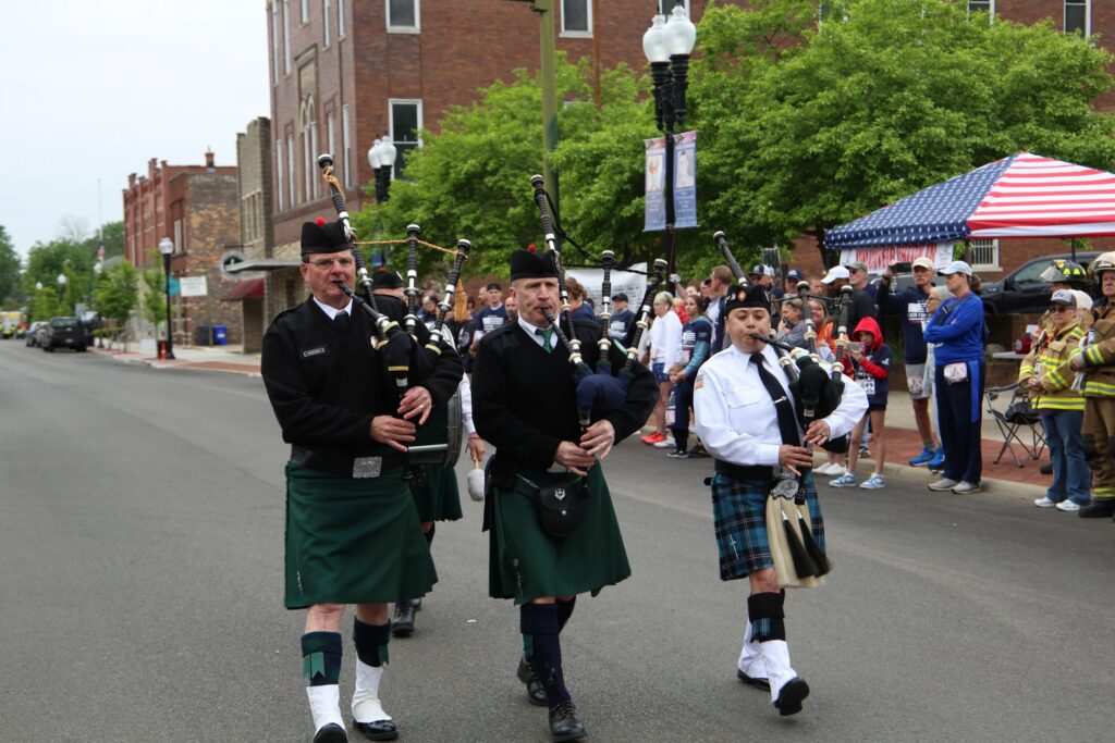 Three bagpipers marching down the street followed by a drummer.