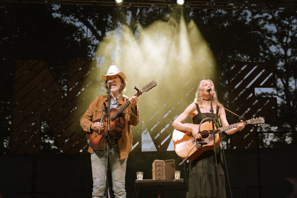 David Rawlings and Gillian Welch perform on stage, holding guitars.