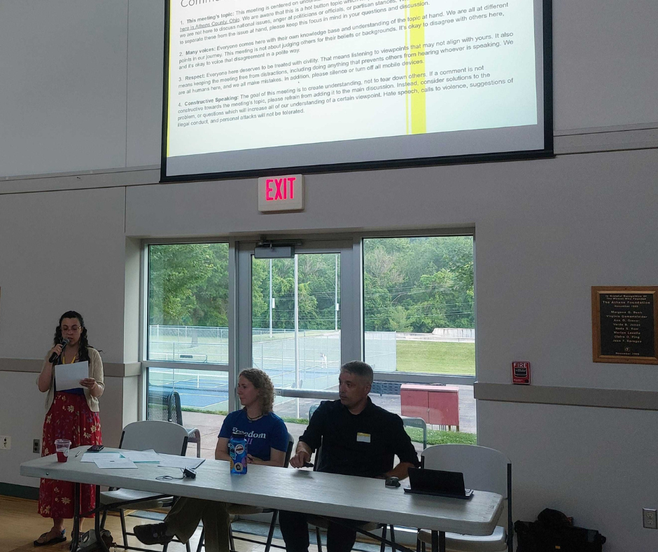 Three people sit at a table before a screen during a presentation.
