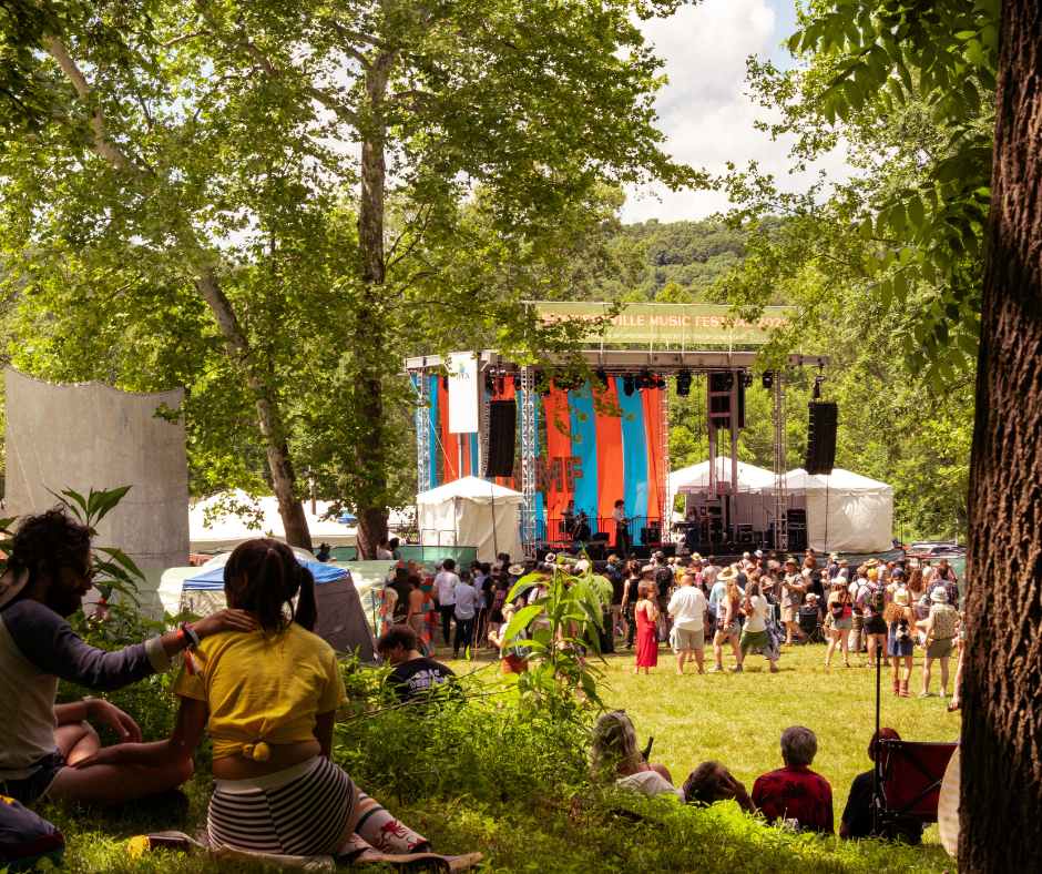 People sit on a hillside facing a crowd standing before a stage.