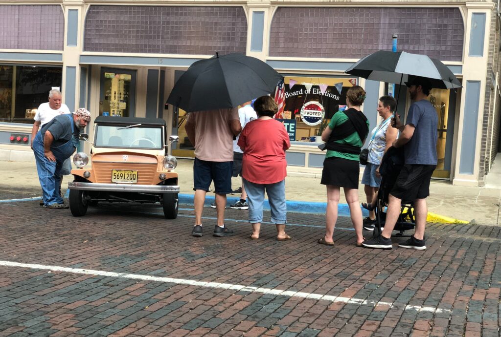 People stand around a King Midget car parked in front of the Board of Elections