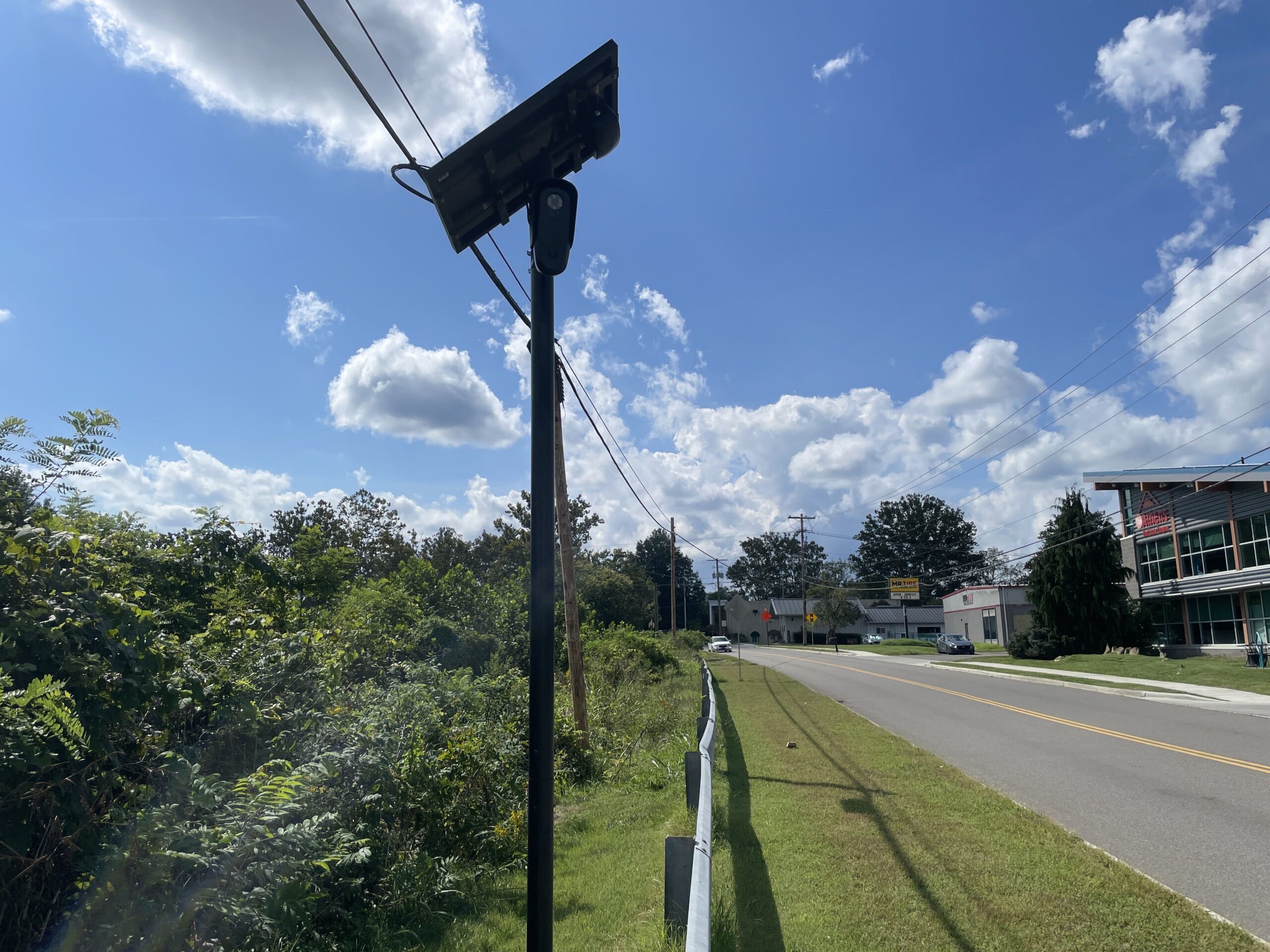 A Flock camera with a solar panel next to a guard rail.
