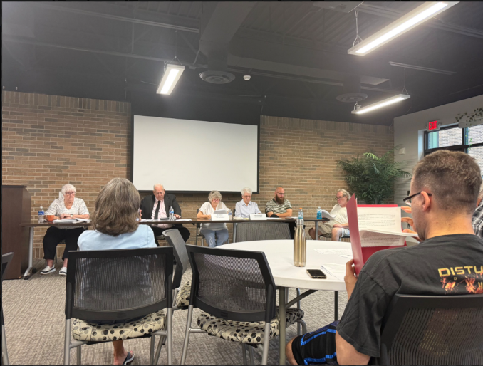 Backs of people in chairs facing people at a table.