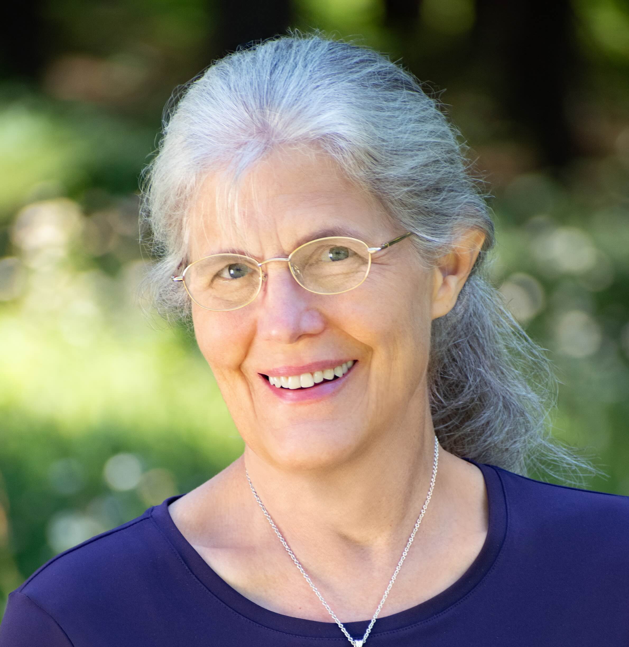 A woman smiling with blurred out wilderness in the background.