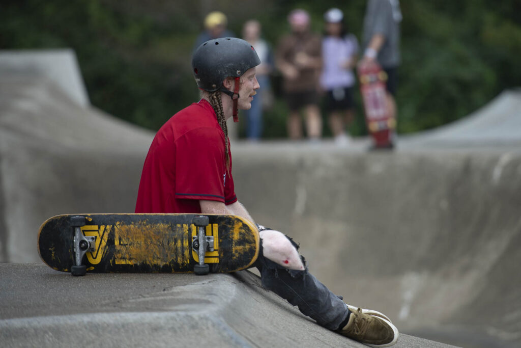 Person sitting in red shirt with helmet on at the rim of skate bowl
