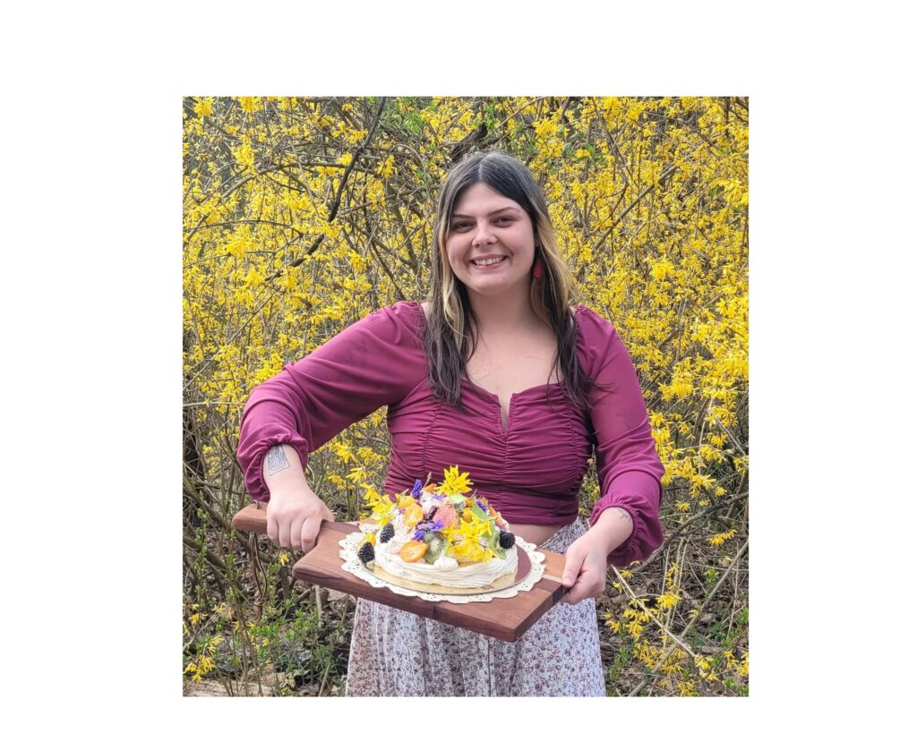 A woman holds up a cake decorated with fruit and flowers.