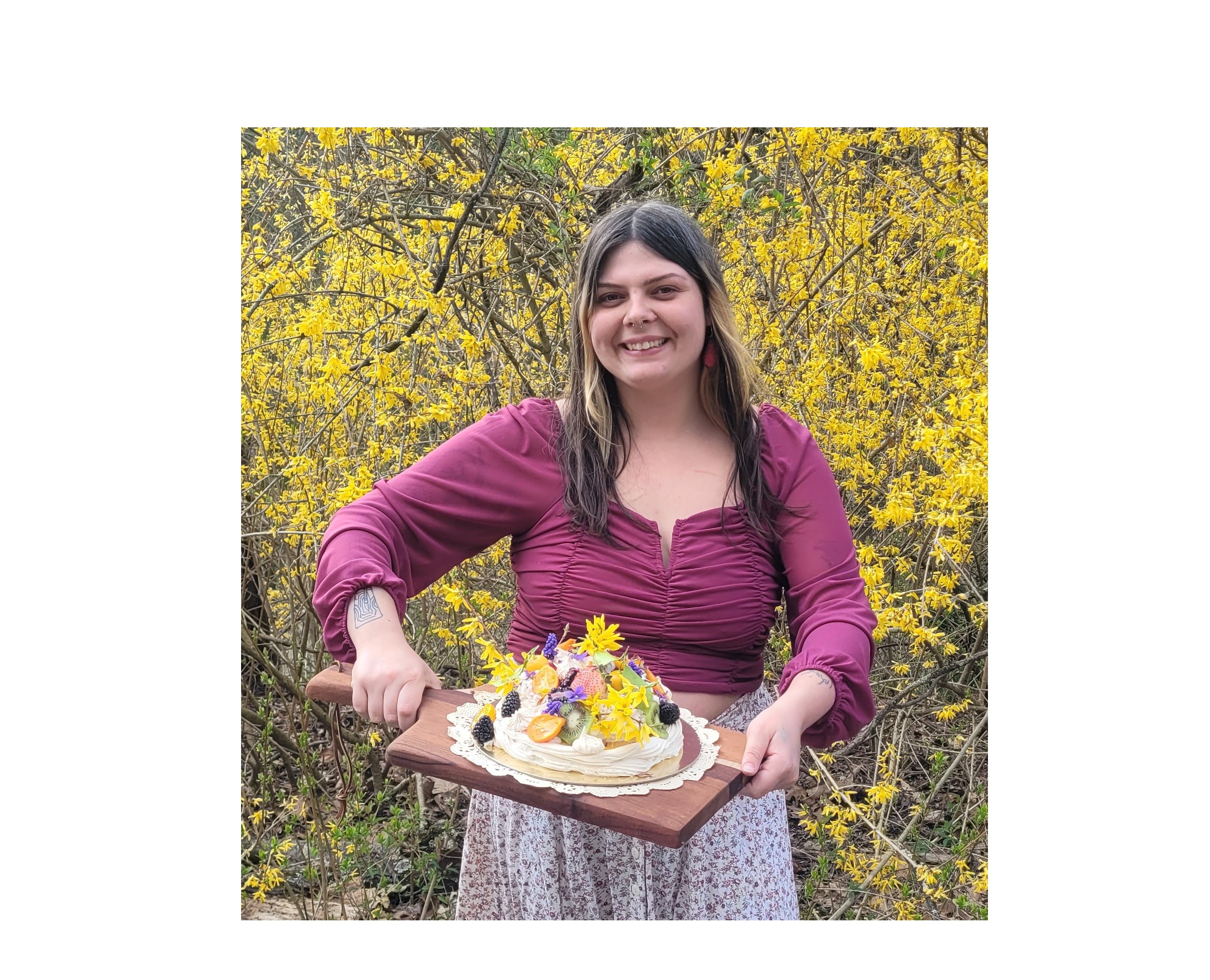 A woman holds up a cake decorated with fruit and flowers.