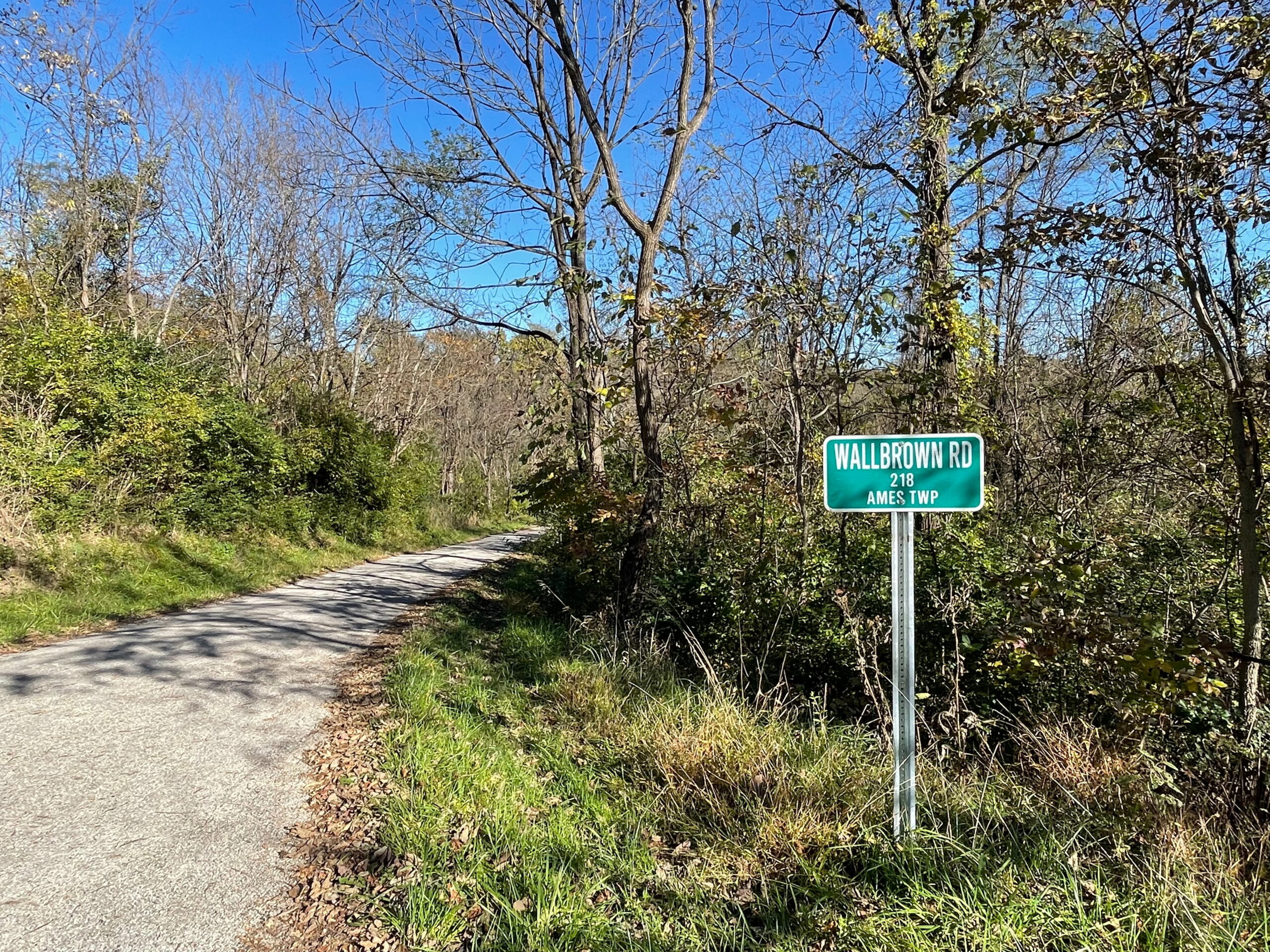A country road pictured under a clear blue sky in fall, with a road sign for Wallbrown Road.