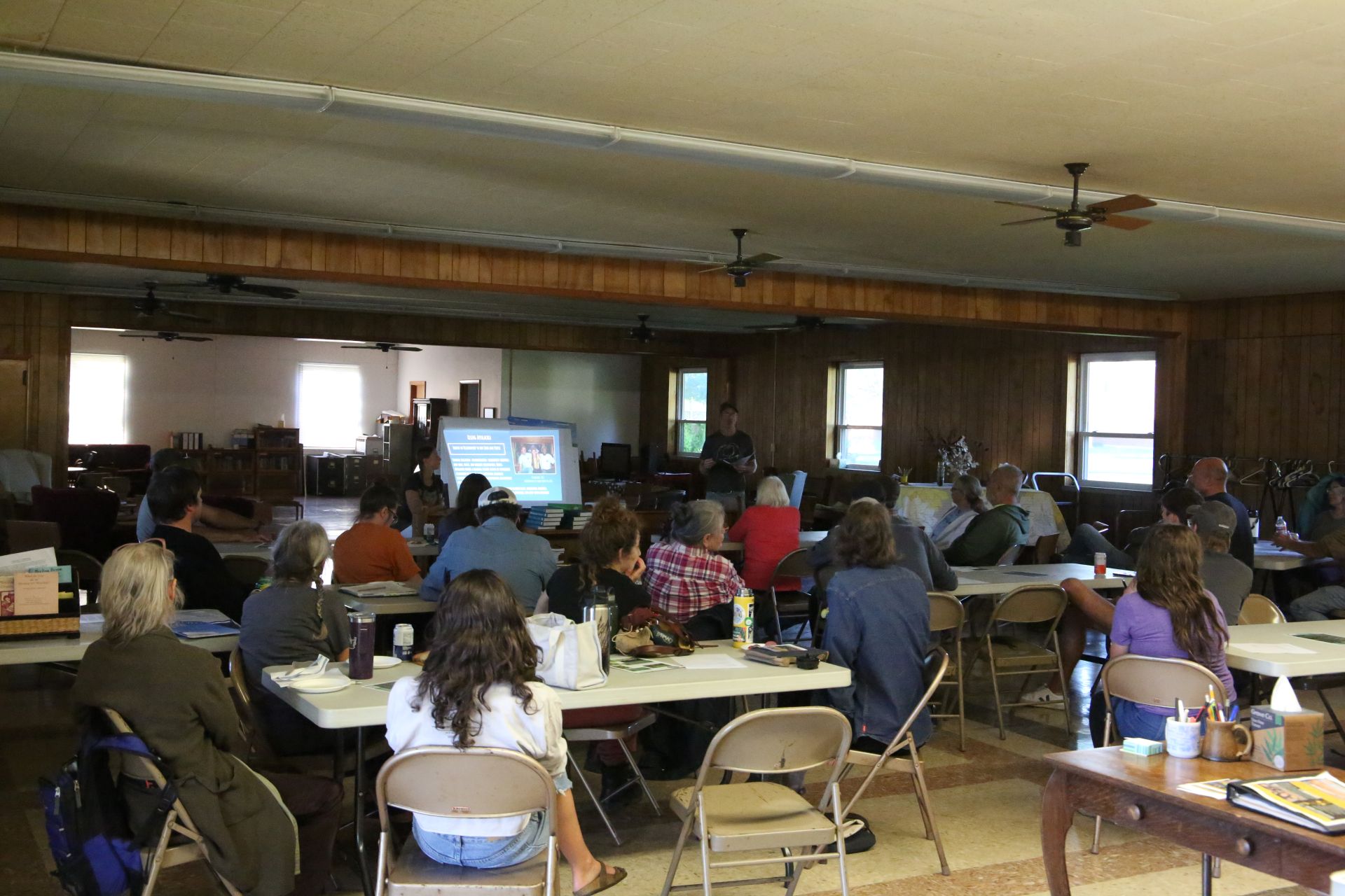 A crowd sits around tables in a meeting hall.